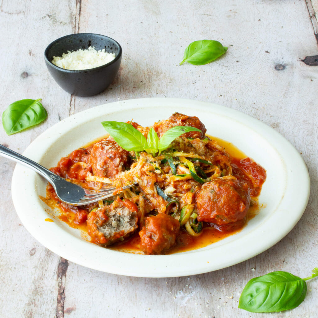 Ein weißer Teller mit Zoodles, Tomatensauce und kleinen Hackbällchen